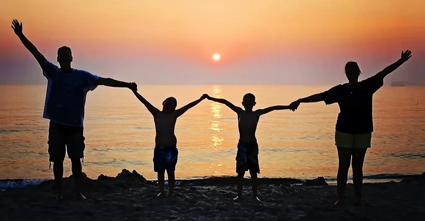 Imagen de familia con puesta de sol al fondo en la playa bienestar familiar técnicas quiropráctica Barcelona